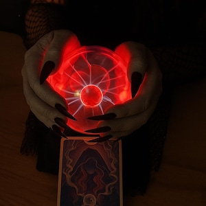 May include: A glowing red plasma ball held in two hands with long, dark fingernails. Below, a tarot card with the text "THE SMOKING VOID" is visible. The image has a mystical, occult theme.