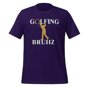 Puede incluir: Camiseta morada oscura con las palabras "GOLFING BRUHz" en blanco y un gráfico de golfista dorado. La camiseta tiene mangas cortas y cuello redondo.