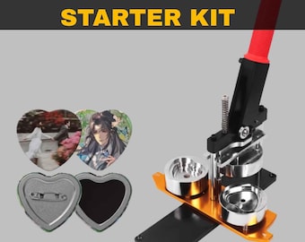 Könnte beinhalten: Ein Herzform-Maker-Starter-Kit mit schwarzer und orangefarbener Basis, rotem Griff und silbernen Formen. Das Kit enthält herzförmige Knopfteile und Beispiele mit gedruckten Bildern. Der Text "Heart Shape Maker STARTER KIT" wird angezeigt.