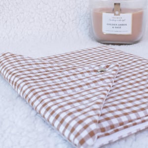 May include: A brown and white gingham pattern cushion with a silver button fastening. A glass candle labelled "Golden Amber & Sage" and a small white ceramic cup are in the background.