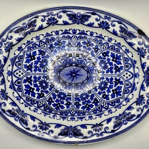 May include: Oval serving platter with a white base and detailed blue floral and butterfly patterns. The rim has a detailed border, and the centre features a symmetrical design. A decorative piece for serving food.