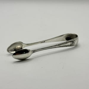 Peut inclure: Pince à sucre en argent avec deux extrémités en forme de cuillère et une poignée décorative. Les pinces sont en métal brillant et réfléchissant et sont conçues pour saisir et soulever les morceaux de sucre. Le design est élégant et classique.