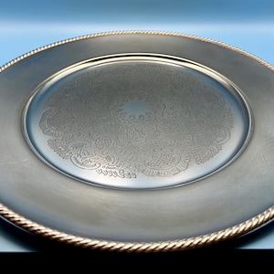 Pode incluir: Uma caneca de cerâmica branca com uma alça preta e o texto "But First, Coffee" em negrito preto. A caneca está sobre um fundo desfocado, sugerindo um ambiente acolhedor. A caneca tem aproximadamente 10 cm de altura.