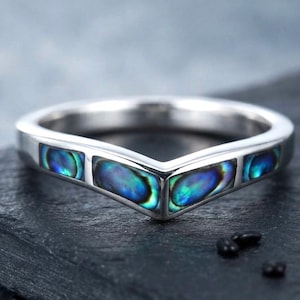 May include: A silver-toned V-shaped ring featuring four rectangular inlays of iridescent abalone shell. The shell displays vibrant shades of blue, green, and purple, set into a polished metal band that forms a distinct chevron point at the centre.