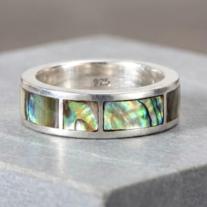May include: A sterling silver band ring featuring a series of rectangular inlays of iridescent abalone shell. The interior of the band is clearly stamped with the number 925, indicating the silver content of this polished metal jewellery piece.