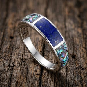 Peut inclure: Une bague argentée dotée d'une incrustation rectangulaire centrale en lapis-lazuli bleu profond avec des éclats dorés, flanquée de deux incrustations rectangulaires plus petites en nacre d'ormeau irisée aux reflets verts, violets et bleus.