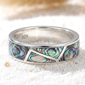 May include: A silver band ring featuring an inlay of iridescent abalone shell with a geometric, segmented pattern. The interior of the band is clearly stamped with the number 925, indicating the sterling silver composition of the jewelry piece.