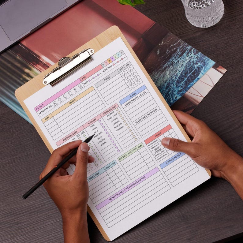 May include: A wooden clipboard with a printed planner sheet. The sheet has sections for patient mood, meals, therapy, and vitals. A person is holding a black pen, writing on the planner. The clipboard has a silver metal clip.