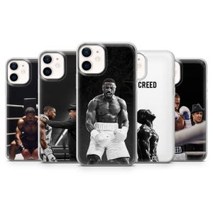 Puede incluir: Una colección de fundas para iPhone con imágenes de la película "Creed". Las fundas muestran fotos en blanco y negro de boxeadores en el ring, con la palabra "CREED" impresa en una de ellas. Las fundas están diseñadas para varios modelos de iPhone.