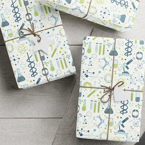 May include: Several wrapped gifts with a science-themed pattern of beakers, molecules, and microscopes in blue, green, and yellow on a white background. The gifts are tied with twine and have blank white tags. A pair of scissors and blank tags are also visible.