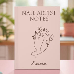 Op de afbeelding: Een lichtroze notitieboek met de tekst "NAIL ARTIST NOTES" in een schreeflettertype. Daaronder staat een lijntekening van een hand met lange nagels en bladeren. De naam "Emma" staat eronder.