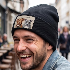 Puede incluir: Un gorro de punto acanalado negro con un parche rectangular en la parte delantera. El parche muestra una ilustración a color de dos perros, uno marrón y otro gris, con el texto "HARLEY & HARPER" impreso en letras mayúsculas negras.