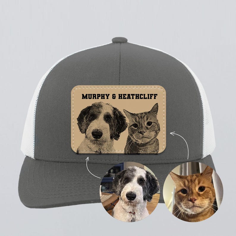 May include: A gray and white trucker hat with a white mesh back. The front features a leather patch with a sepia-toned portrait of a dog and a cat, and the text "MURPHY & HEATHCLIFF". Below are two circular pet portraits.