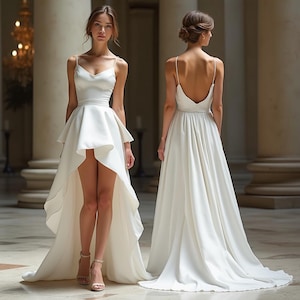 Peut inclure: Une robe de mariée blanche avec une jupe asymétrique et des bretelles fines. La robe présente un corsage ajusté et une traîne fluide. Le modèle porte des talons nude. L'arrière-plan comprend des colonnes et un lustre.