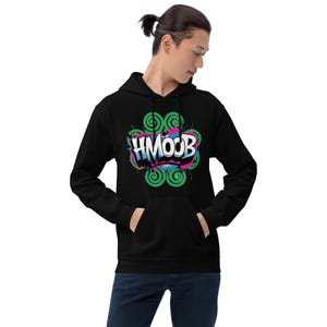 May include: Black hooded sweatshirt with a front pocket and a vibrant graphic. The design includes the word "HMOOB" in white, encircled by green swirls and splashes of pink and blue. The sweatshirt is made of a soft material.