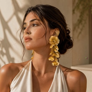 May include: A pair of gold-toned drop earrings featuring a cascading design of multiple textured, layered flower petals. The earrings have a metallic finish and hang vertically from the earlobe, creating a long, dangling silhouette.