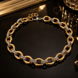 Puede incluir: Un collar de cadena bicolor que presenta una alternancia de eslabones ovalados dorados lisos y eslabones plateados texturizados. El collar incluye un cierre de mosquetón y una cadena extensora ajustable con pequeños eslabones circulares.