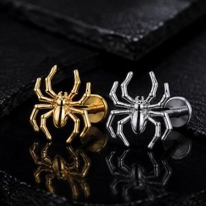 Peut inclure: Deux boucles d'oreilles en forme d'araignée, l'une dans un ton doré poli et l'autre dans un ton argenté poli. Chaque boucle d'oreille présente un corps d'araignée détaillé avec huit pattes pliées et une tige plate circulaire à l'arrière.