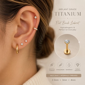 May include: A close-up of an ear adorned with gold-colored jewelry, including a hoop earring, a cartilage cuff, and several stud earrings with clear gemstones. The image also features a gold labret stud with a clear gemstone. Text reads "IMPLANT GRADE TITANIUM".