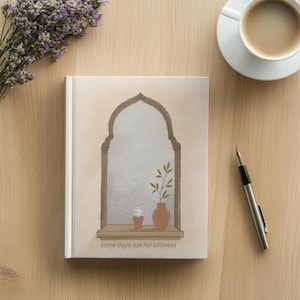 Peut inclure: Un carnet à couverture rigide beige clair illustré d'une fenêtre en arc, d'un petit vase en terre cuite avec une plante et d'une minuscule tasse. Le texte "some days ask for stillness" est imprimé en petites lettres marron foncé en bas.
