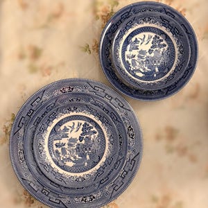 Puede incluir: Un juego de platos azules y blancos con diseño Willow. Los platos presentan una escena detallada de paisaje en el centro, rodeada por un borde decorativo. El juego incluye platos de varios tamaños, perfectos para servir una comida.