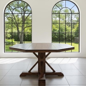 Könnte beinhalten: Ein großer, achteckiger Esstisch aus Holz mit dunkelbraunem Finish. Der Tisch hat ein stabiles Gestell im Sockelstil. Der Raum verfügt über große Bogenfenster mit Blick auf Bäume und Grün sowie einen Kamin.