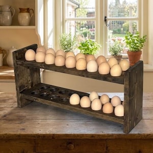 May include: A rustic, two-tiered wooden egg holder, stained dark brown, filled with fresh eggs. The holder has a slanted design for easy access and display. The eggs are light brown and arranged neatly on the shelves.