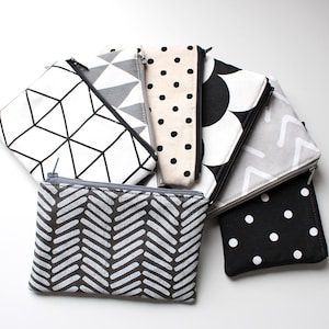Könnte beinhalten: Ein Set mit sieben schwarzen und weißen gemusterten Reißverschlusstaschen. Die Taschen sind aus Stoff und haben verschiedene geometrische Muster.