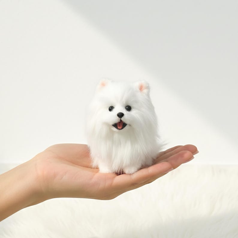 Op de afbeelding: Een pluizig, wit Pomeriaan hondenbeeldje met zwarte ogen en een roze tong. De kleine hond zit op een hand en toont zijn zachte, pluche vacht. De achtergrond is effen wit.
