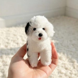 Op de afbeelding: Een kleine pluche hond met witte vacht en zwarte vlekken op de oren en het lichaam. Het knuffeldier heeft een zwarte neus, donkere ogen en een klein rood tongetje dat zichtbaar is tussen de bek. Het speelgoed heeft een zachte, pluizige textuur.