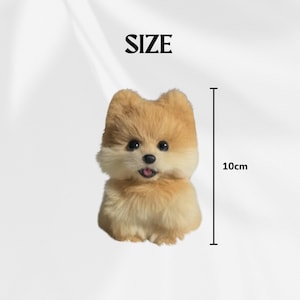 Op de afbeelding: Een pluche Pomeranian hond figuur, voornamelijk bruin en cr&egrave;me van kleur, met zwarte ogen en een roze tong. De figuur is ongeveer 10 cm hoog. Het woord "SIZE" staat boven de hond.