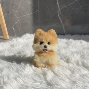 Op de afbeelding: Een pluche Pomeranian hondenspeelgoed met bruin en cr&egrave;mekleurig haar, zwarte ogen en een licht geopende mond. Het speelgoed staat op een witte, pluizige vloerkleed. Een schattig en knuffelbaar item.