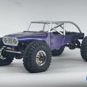 May include: A purple metallic remote-controlled rock crawler vehicle featuring a silver roll cage, large black off-road tires with chrome rims, and a front grille with circular headlights. A blue circular logo with the text 4.0 MICRO is visible.