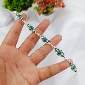 May include: A silver-toned bracelet featuring five round, faceted green stones set in ornate metal frames. The links are connected by small silver rings, creating a delicate chain design that showcases the vibrant green color of the stones.