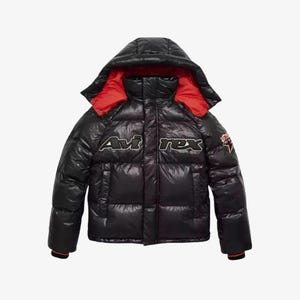 Puede incluir: Chaqueta acolchada negra con capucha y forro rojo. La chaqueta presenta el texto "Avi Rex" en blanco y negro en el pecho. Un peque&ntilde;o parche es visible en la manga derecha. La chaqueta tiene un acabado brillante.