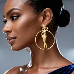 May include: Gold hoop earrings with a figure design. The earrings are large and circular, with a detailed silhouette of a person. The figure is positioned within the hoop, creating a unique and elegant accessory.