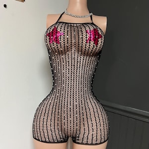 May include: Black fishnet romper with a halter neck and shorts. The romper is embellished with small, sparkling rhinestones. The bust area features two pink flower-shaped pasties. A silver chain necklace completes the look.