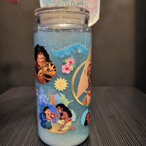 Puede incluir: Un tarro de cristal transparente con tapa, lleno de l&iacute;quido azul y purpurina. El tarro est&aacute; decorado con pegatinas de personajes de dibujos animados de colores. El texto "Ashley's Beautiful Customs" es visible en una pegatina circular.