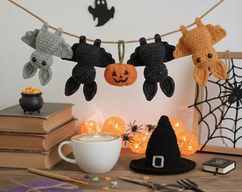 May include: A Halloween-themed display featuring crocheted bats, a pumpkin, and a witch's hat. A cup of coffee sits on a wooden surface with books, a small cauldron, and decorative lights. A spider web and a ghost silhouette are in the background.