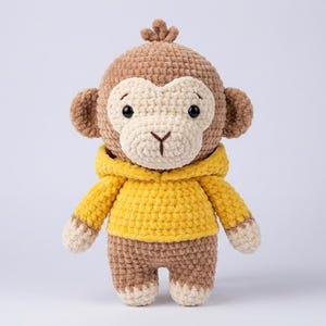 May include: A handmade crochet monkey doll in shades of brown, beige, and yellow. The monkey has a brown head, ears, and body, with a beige face and hands. It is wearing a yellow hooded sweatshirt. A cute and cuddly stuffed animal.
