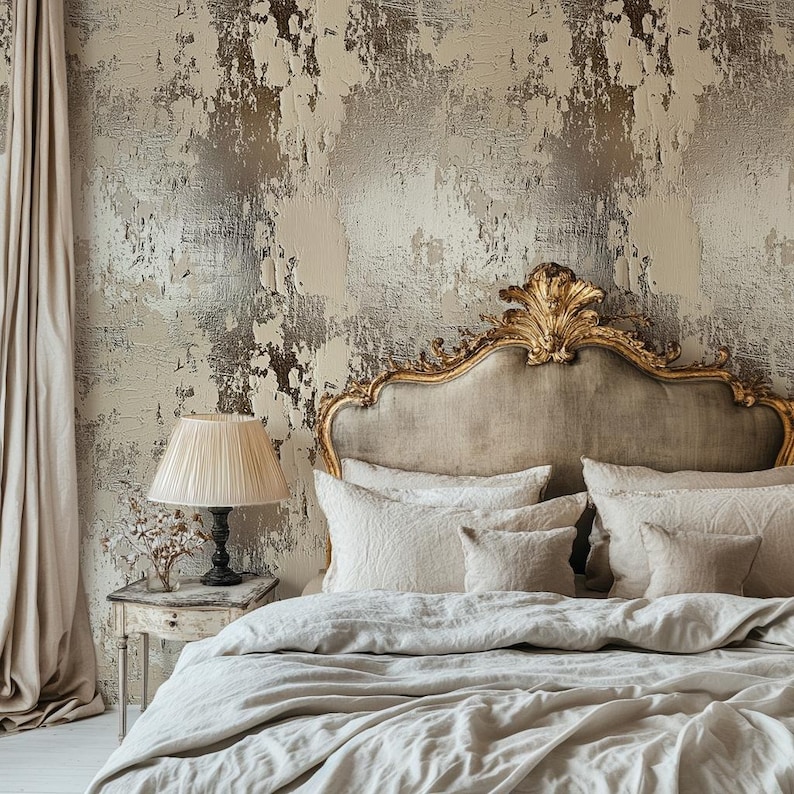 May include: A bedroom scene featuring a bed with a gold-framed headboard, cream-colored bedding, and decorative pillows. A bedside table with a lamp and a textured wall with a distressed finish complete the elegant decor.