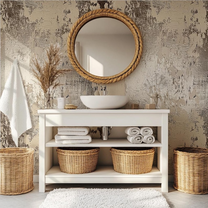 May include: A bathroom vanity with a white countertop, a round mirror with a rope-like frame, and a white sink. The vanity has shelves with folded white towels, woven baskets, and a white rug. The background is a textured wall.