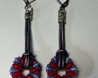May include: A pair of dangle earrings with a purple leather cord and a red and purple beaded circle pendant.