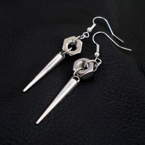 May include: A pair of silver earrings with a pointed spike and a hexagonal nut. The earrings are made of metal and have a simple design.