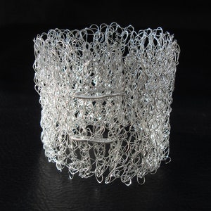 May include: A silver wire bracelet with a delicate, intricate design. The bracelet is made of many small loops of wire that are woven together to create a textured, openwork pattern.