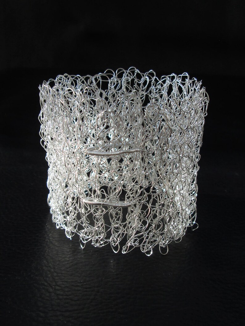 May include: A silver wire bracelet with a delicate, intricate design. The bracelet is made of many small loops of wire that are woven together to create a textured, openwork pattern.