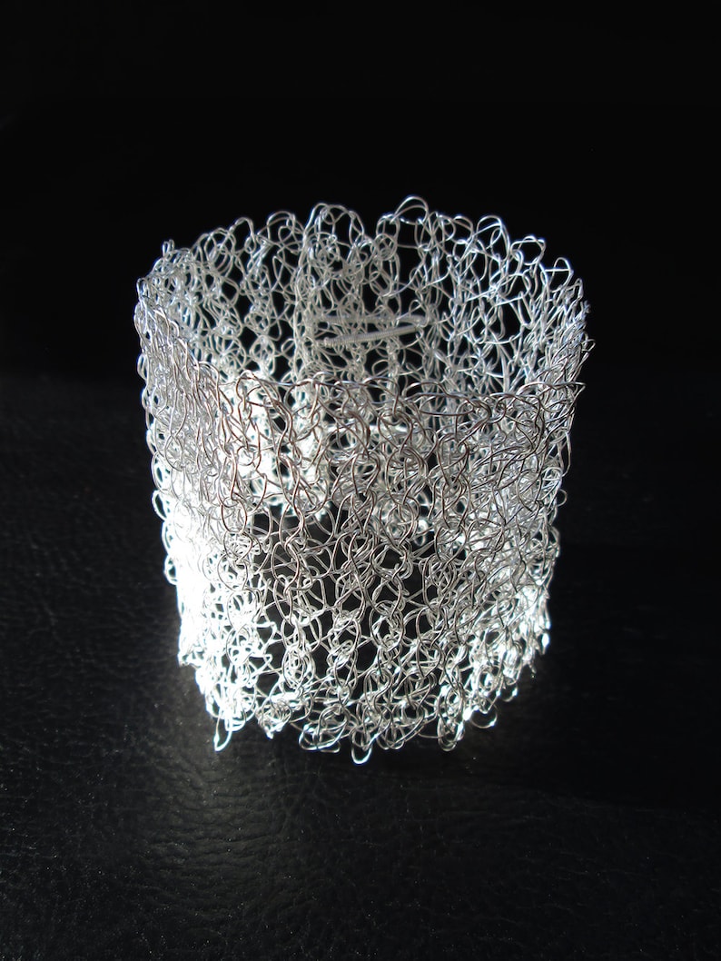 May include: A silver wire bracelet with a delicate, intricate design. The bracelet is made of a fine mesh of wire, creating a delicate and airy look.