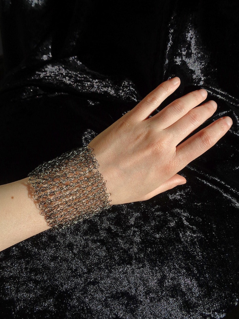 May include: A silver chainmail bracelet on a person's wrist. The bracelet is made of small, interconnected metal rings.