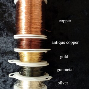 May include: Five spools of wire in different colors: copper, antique copper, gold, gunmetal, and silver. The spools are stacked on top of each other.
