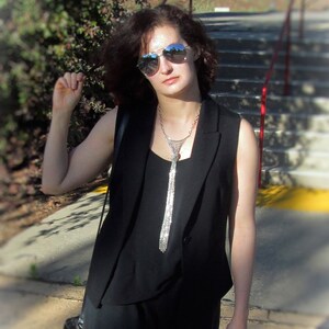 Puede incluir: Una mujer con un chaleco negro sin mangas, un collar de cadena plateada y gafas de sol. Est&aacute; de pie en una escalera.